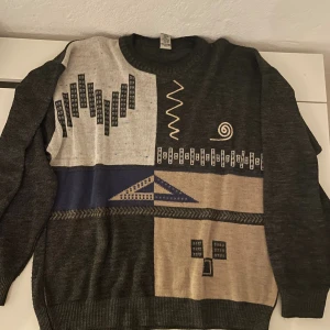 Mönstrad stickad tröja - Unik stickad tröja med coolt grafiskt mönster i svart, beige, grått och blått. Perfekt för dig som gillar vintagevibbar och statement-plagg. Mycket bra skick, storlek S.
