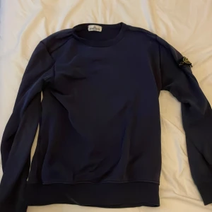 Mörkblå sweatshirt från Stone Island - Säljer en stilren mörkblå sweatshirt från Stone Island Junior. Tröjan har rund halsringning, långa ärmar och den klassiska loggan på vänster ärm. Perfekt för dig som gillar streetwear och vill ha något snyggt och bekvämt. Tröjan e 100% äkta och köpt på NK