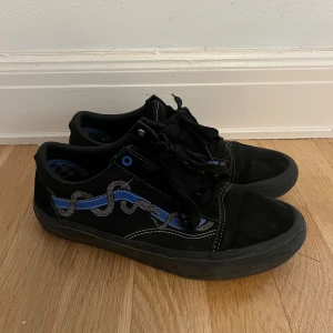 Svarta Vans sneakers med blå detalj - Säljer ett par svarta Vans sneakers med blå och grå vågig detalj på sidan. Skorna har snörning, svarta sulor och klassisk låg profil. Materialet är en mix av mocka och syntet, med schackrutigt mönster på insidan. Perfekta för skate eller streetstyle. Obs ingen original box 