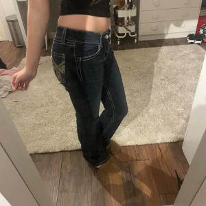Mörkblå bootcut jeans med broderi - Säljer ett par mörkblå jeans med bootcut passform och snygga kontrastsömmar. Jeansen har broderade detaljer på bakfickorna och sitter lågt i midjan. Storlek 158 och säljer för att dom är för små!