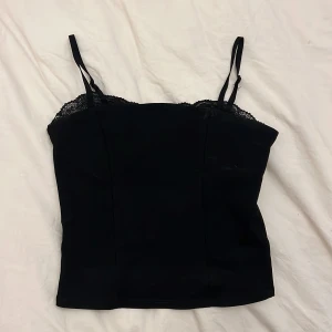 Svart linnetopp med spets från Amisu - Snygg svart linnetopp från Amisu i storlek XS. Toppen har tunna justerbara axelband och spetsdetaljer längs överkanten som ger en extra touch. 