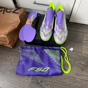 Adidas F50 lila fotbollsskor - Säljer ett par Adidas F50 fotbollsskor i lila och neongult. Skorna har en strömlinjeformad design med F50-tryck på sidan och levereras med matchande skopåse och extra innersulor. Perfekta för dig som vill sticka ut på planen.