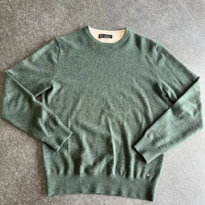 Grön stickad merinoull tröja  - Mysig grön stickad tröja från Lagency med rund halsringning och ribbade muddar. Tröjan har en diskret metallogo vid nederkanten och är perfekt för lager-på-lager. Passformen är normal och materialet känns mjukt och värmande. Storlek M, nypris 1200kr. (Enda defekt är att lilla metall loggan behövts sättas fast igen med en liten tråd).