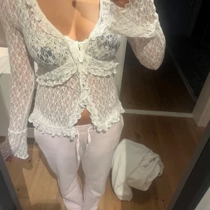 Vit spetsblus med volang och knyt från BikBok - Säljer en superfin vit blus i spets med långa ärmar och volangdetaljer. Blusen har knyt framtill och är genombruten med romantisk känsla. Perfekt för dig som gillar feminina och trendiga plagg. Snygg att styla över ett linne eller bralette.