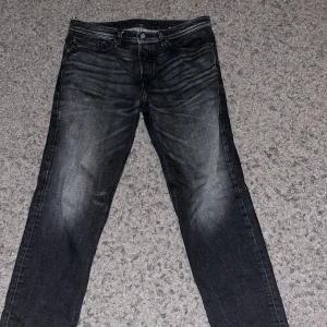 Svarta jeans från Diesel W32 - Snygga svarta jeans från Diesel med cool tvättad look och klassiska fem fickor. Jeansen har raka ben och tydliga slitningar för en trendig vibe. Perfekta för dig som gillar streetstyle och vill ha ett par jeans som sticker ut. 32/32