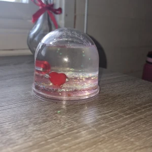 Glittervattenprydnad med hjärtan - Dekorativ glittervattenprydnad med röda hjärtan inuti och glittrande partiklar. Perfekt som present eller bordsdekoration. Produkten är i gott skick utan synliga skador eller slitage. Ej elektronik.