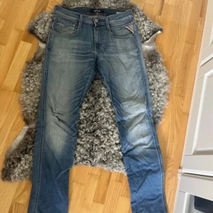 Blå Replay jeans med slitningar - Snygga blå jeans från Replay med klassisk femficksdesign och slitna detaljer på benen. Jeansen har raka ben och normal passform, med ljus tvätt och diskreta slitningar för en cool look. Perfekta för dig som gillar en avslappnad stil. Storlek 29