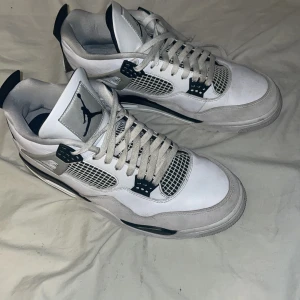 Nike Air Jordan 4 vit/svart/grå - Säljer ett par Nike Air Jordan 4 i vitt, svart och grått. Skorna har klassisk meshpanel, snörning och den ikoniska Jumpman-loggan på plösen och hälen. Ovandelen är i skinn med detaljer i syntet och mesh. Perfekta för dig som vill sticka ut med en tidlös sneaker.