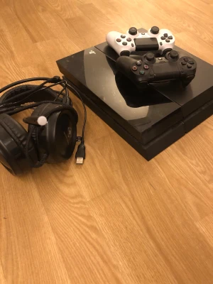 PlayStation 4 med två kontroller och headset - Säljer en PlayStation 4 med två DualShock 4-kontroller (svart och vit), headset med USB-anslutning samt nödvändiga kablar. Köpte hörlurarna för 500:- ny pris. Kan ta bort hörlurarna och 500:- om man inte vill ha dom. Kan sänka priset vid snabb affär 