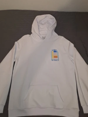 Vit hoodie från Casablanca - Vit hoodie från Casablanca med färgglatt tryck av ett fönster och texten 'Casa Blanca' på bröstet och ryggen. Tröjan har huva och känguruficka, perfekt för dig som gillar stilrena men ändå unika plagg