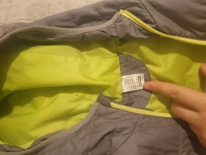 Grå quiltad pufferjacka Decathlon - Quiltad pufferjacka från Decathlon i grått med ljusgul insida och detaljer. Jackan har huva, två fickor med dragkedja och hel dragkedja framtill. Perfekt för kyliga dagar och har en sportig vibe. Materialet är polyester och passformen är normal.