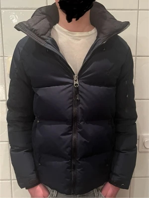 Mörkblå pufferjacka från Polo Ralph Lauren - Säljer en mörkblå pufferjacka från Polo Ralph Lauren i storlek XS. Jackan har hög krage, huva och grov dragkedja framtill. Fylld med dun och har en clean, oversized look som är perfekt för kalla dagar. Snygg och enkel design med diskret logga på bröstet. Skicket är bra med ytterst lite skavanker. Bild kan fås om det önskas! Köpt i Ralph Lauren butik.