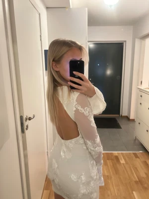 Vit kort klänning med öppen rygg - Min kära studentklänning med blommiga spetsdetaljer. Klänningen är öppen rygg och volang vid ärmsluten. Skriv för fler bilder😇 