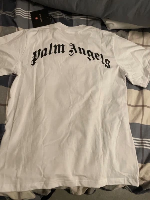 Palm Angels vit t-shirt med björntryck - Palm Angels t-shirt i vitt med stort svart logotryck på ryggen och ett unikt björntryck på framsidan. T-shirten har rund hals och korta ärmar. Har fått i present men aldrig använt både påse och etikett finns kvar,  lägre pris  pga osäkerhet omkring märket(äkthet). Tjockare material och bra kvalitet.