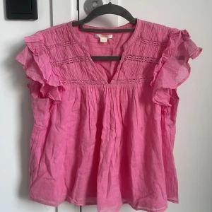 Rosa blus med volang 🩷 från Gina Tricot - Supersöt rosa blus från Gina Tricot i luftig bomull. Blusen har volangiga korta ärmar, v-ringning och fina broderade detaljer upptill. Perfekt för dig som gillar en romantisk och lekfull stil. Säljes i storlek 158/164. Den har några fläckar på sig!!
