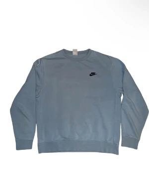 Nike sweatshirt  - Ljusblå sweatshirt från Nike i storlek S. Tröjan har klassisk rund hals, långärmade ärmar och en liten svart Nike-logga på bröstet. Tillverkad i mjuk bomull med ribbade muddar vid ärmslut och nederkant. Perfekt för chill dagar eller när du vill ha en clean look. 