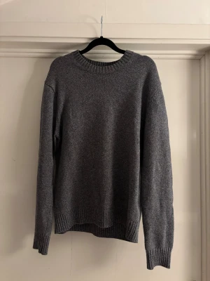 Grå stickad tröja från Massimo Dutti - Säljer en stilren grå stickad tröja från Massimo Dutti i 100% bomull. Tröjan har rund hals, ribbade muddar vid ärmslut och nederkant samt långärmad passform. Perfekt för dig som gillar enkel och klassisk look. Passar M