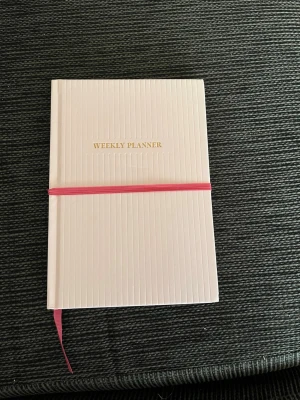 Veckoplanerare  - Stilren och modern veckoplanerare i ljusrosa med rosa band. Perfekt för dig som vill ha koll på veckan, planera dina to-dos och anteckna viktiga saker. Passar dig som gillar struktur och vill boosta din produktivitet på ett snyggt sätt. Enkel att ta med i väskan och perfekt för studenter och unga vuxna.