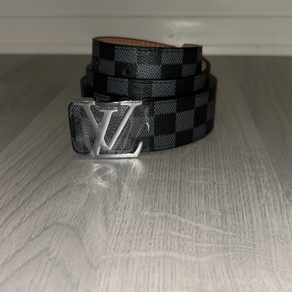 Ett svart bälte med silver logga från Lindex