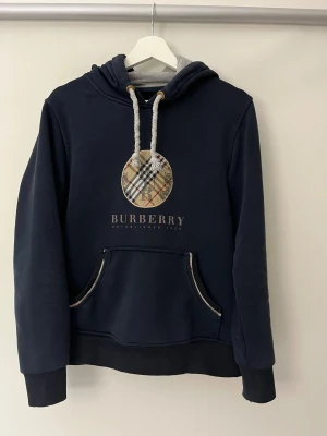 Burberry - Mörkblå burberry hoddie med tjocka snören och luva. Stilen på tröjan är lite vintage men den funkar med nästan varje outfit. Bara att höra av sig vid frågor.