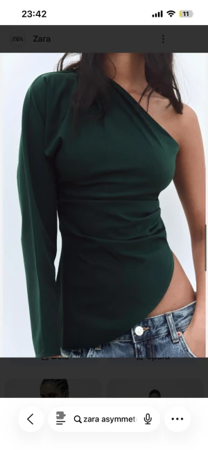 Mörkgrön oneshoulder topp från Zara - Snygg mörkgrön topp från Zara med asymmetrisk design och oneshoulder. Toppen har en lång ärm på ena sidan och är axelbandslös på andra, vilket ger en cool och modern look. Passar perfekt till jeans eller kjol för en trendig outfit. Gick ner i vikt så den passar ej längre❤️ Helt ny, aldrig gått ut med den.