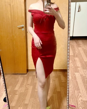 VinRöd offshoulder klänning med slits - Snygg röd klänning med offshoulder-design och figurnära passform. Klänningen har en markerad v-ringning och en hög slits framtill som ger en cool touch. Materialet är slätt och har en lätt glans. Perfekt för dig som vill sticka ut med en elegant och modern look.