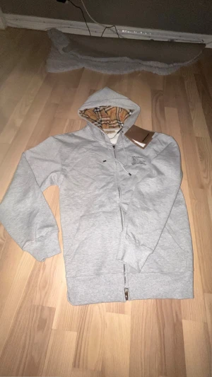 Grå Burberry zip up hoodie  - Säljer min gråa Burberry zip up hoodie. Den passar mig otroligt bra då jag har storlek S och hoodien är storlek S men den skulle passa folk med XS och M.