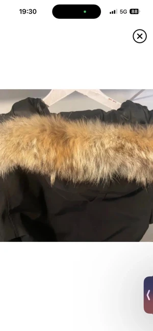 Päls päls päls - Svart parkas med fluffig beige-brun päls runt huvan. Jackan har en klassisk form och är perfekt för kalla dagar. Pälsen ger en snygg kontrast mot det svarta tyget och gör jackan extra mysig och trendig.