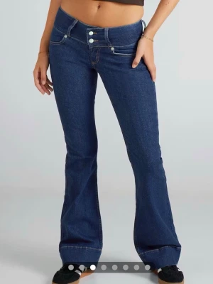 Lågmidjade blå jeans  - Säljer dessa Lågmidjade blå jeans, de har två knappar vid midjan och detalj vid benen. Knappt använda. 
