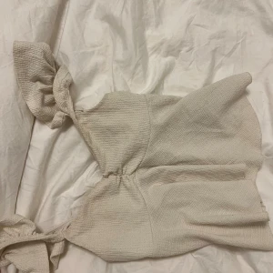 Beige ärmlös linnetopp med knyt - Supersöt beige linnetopp med knyt på axlarna och lätt strukturerat tyg från gina tricot. Toppen är ärmlös och har en lätt croppad passform som ger en avslappnad men ändå chic vibe. Perfekt att styla med jeans eller kjol för en trendig look.