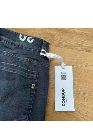 Mörkgrå jeans från Dondup - Säljer ett par mörkgrå jeans från Dondup med snygg tvätt och klassisk femficksdesign. Jeansen har raka ben och normal passform, med diskret D-detalj på bakfickan. Tillverkade i mjukt bomullsjeansmaterial för en skön känsla. Aldrig använda!