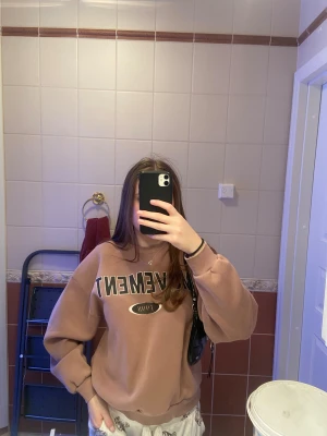 Brun/lila sweatshirt  - Säljer en brun sweatshirt från Movement med trycket 'Movement 1998' i svart och vitt på bröstet. Tröjan har rund hals, ribbade muddar och lång ärm. Perfekt för chill dagar och enkel att matcha med jeans eller mjukisbyxor.