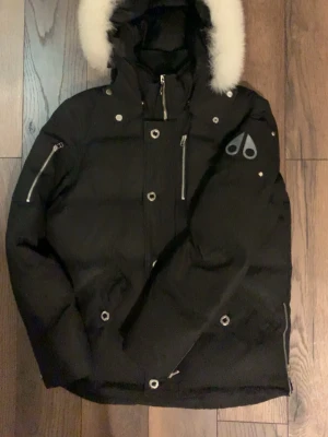 Moose Knuckles Jacka - Jackan är i fint skick inga större fläckar finns dock lite slitage på jackan men inget som är svårt att fixa och som syns. Jackan är fräsch och pälsen är i väldigt bra skick och ser inte konstig ut eftersom jag i princip aldrig hade luvan på.  Det är en Storlek M men om man är storlek S passar den också väldigt bra speciellt med en hoodie eller tröja under. Jag är osäker på om jackan är äkta men jag antar att den är det från vad jag kollat kan inte garantera .Skriv om ni undrar något.