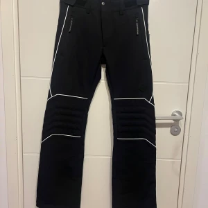 Skidbyxor, J.Lindeberg - Svarta skidbyxor, med vita detaljer från J.Lindeberg i storlek S. Oanvända med lappen kvar. Klassas som softshell-byxor.