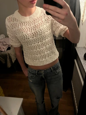 Vit stickad croppad topp - Säljer en vit stickad croppad topp med korta ärmar och rund hals. Toppen har ett luftigt, hålstickat mönster. Från Amisu men sälj ej längre.