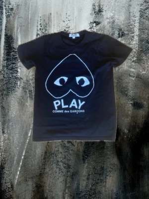Svart Comme des Garçons Play t-shirt - Svart t-shirt från Comme des Garçons Play med ikoniskt hjärta med ögon tryckt på bröstet och texten PLAY. Klassisk passform, rund hals och korta ärmar. Tillverkad i mjuk bomull, perfekt för en clean och cool streetstyle. Passar ca 170-180 skriv om du har frågor!