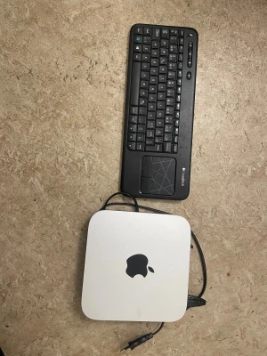 Apple Mac mini - Apple Mac mini stationär dator i silver med tillhörande Logitech trådlöst tangentbord med inbyggd touchpad. Viss yttre kosmetisk slitage syns på chassit, men överlag i gott skick. Perfekt för kompakt arbetsstation eller mediacenter.