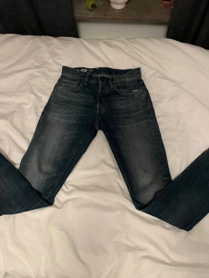 Mörkblå G-Star jeans tapered fit - Snygga mörkblå jeans från G-Star med klassisk femficksdesign och diskret logga på fickan. Modellen har tapered fit med smalare ben och normal midja. Jeansen är tillverkade i slitstarkt denim och har snygga tvättade detaljer för en cool look. Dem är använda 2 gånger och är helt nya och fräscha. W28 L32