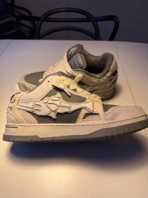 Vicinity skor storlek 42.5 ”AKIMBO LOWS V2 "MOON ROCK" - Snygga sneakers från Vicinity i grått och vitt. Skorna har tjocka vita snören, perforerad tå och vadderad plös med logga. Materialmix av mocka och syntet ger en unik look. Perfekt för dig som vill sticka ut med streetwear. Nypris 2300kr