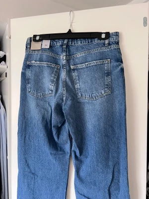 Blå jeans från märket Rebel, storlek 34 - Snygga blå jeans från Rebel med klassisk femficksdesign och knappgylf. Jeansen har en rak passform och är perfekta för en avslappnad stil. De har en lätt tvättad look som ger en cool vintagekänsla. Lågmidjade. Aldrig använda, prislappen kvar. Önskar du veta exakta mått? Tveka inte att höra av dig!