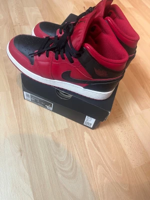 Nike Air Jordan 1 mid svart/röd sneakers storlek 39 - Säljer ett par ikoniska Nike Air Jordan 1 sneakers i svart och rött skinn med vita sulor. Klassisk mid modell med svart snörning och rund tå. Perfekta för dig som vill ha en streetstyle-vibe och gillar retroinspirerade sneakers. Skorna har storlek 39 och skokartongen finns med + crease skydd. Skorna är nästan aldrig använda och i perfekt form.