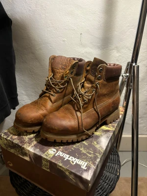 Bruna Timberland boots med snörning - Säljer ett par klassiska bruna Timberland boots med grov sula och snörning. Skorna är tillverkade i slitstarkt skinn och har rund tå samt vadderad krage för extra komfort. Perfekta för höst och vinter, med robust design och ikonisk Timberland-logga på sidan. Storlek 42, ny pris 2500kr mitt pris 599kr ✅. Lådan tillkommer vid köp.  Hör av dig vid funderingar📩