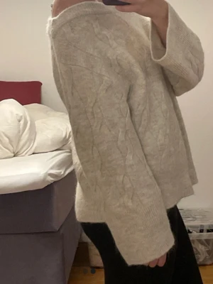 Beige stickad offshoulder tröja - Supermysig beige stickad tröja med bred offshoulder-ringning och kabelstickat mönster. Tröjan har långa ärmar och en loose fit som ger en chill vibe. Perfekt att slänga på sig när det är kallt ute.