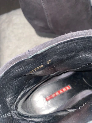 Svarta mockaboots från Prada, storlek 37 - Säljer ett par svarta boots från Prada i storlek 37. Skorna är tillverkade i mjuk mocka med en plattformsula och har en stilren, minimalistisk design. Insidan är fodrad med skinn och de har en spetsig tå som ger en snygg siluett. Perfekta för dig som gillar exklusiva märken och klassisk stil.