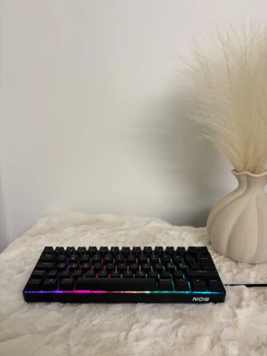 NOS KR200 RGB Mekaniskt Tangentbord - NOS KR200 är ett kompakt mekaniskt tangentbord med RGB-belysning. Perfekt för gaming eller arbete, med nordisk layout och snygg design. Tangentbordet är i mycket fint skick utan synligt slitage. Ansluts via kabel för stabil prestanda.