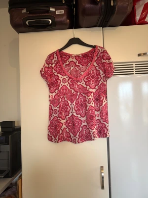 Rosa och vit blus med mönster - Säljer en söt blus med korta ärmar och v-ringning. Blusen har ett detaljerat rosa och vitt mönster som ger den en unik vibe. Materialet känns lätt och luftigt, perfekt för varmare dagar. Passformen är normal och toppen har en fin rynkdetalj under bysten. Från märket Odd Molly. Storlek 2 som enligt deras storleksguide motsvarar en M. Men den ör någon liten i storlek. Mycket fint skick, jag hittar inga synliga anmärkningar eller defekter. 