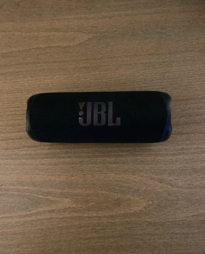 JBL Flip 6 - JBL Flip 6 bärbar Bluetooth-högtalare i svart. Kompakt design, tydlig JBL-logga, USB-C-laddning och robust konstruktion. Några mindre repor och slitage syns på sidorna, men i gott skick. Perfekt för musik på språng med kraftfullt ljud och lång batteritid.