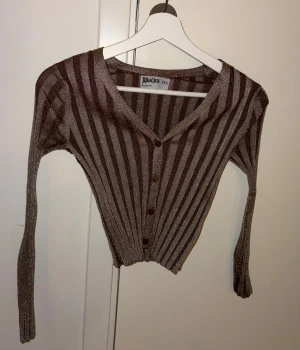 Glittrig randig kofta Rita Ora x Primark - Glittrig kofta med bruna och beige ränder från Rita Ora x Primark. Modellen har v-ringning och knappar framtill. Materialet är stretchigt. Mycket bra skick. 