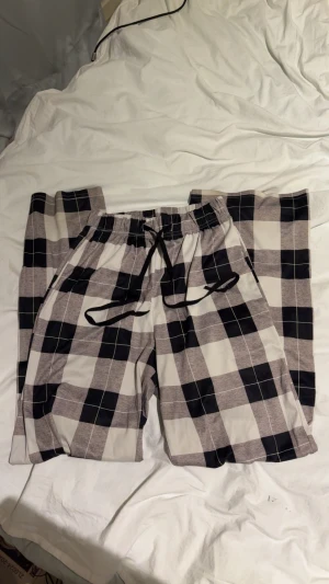 Rutig mjukisbyxa med snörning - Säljer ett par chillade mjukisbyxor med svart och grått rutmönster. De har elastisk midja och svart snörning framtill för extra komfort. Perfekta för att hänga hemma eller dra till gymmet. Materialet känns mjukt och skönt mot huden.
