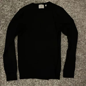 Svart stickad tröja från Bläck - En stilren svart stickad tröja från Bläck i storlek S. Tröjan har rund halsringning och långa ärmar med ribbade muddar. Perfekt för dig som gillar en clean och enkel look.